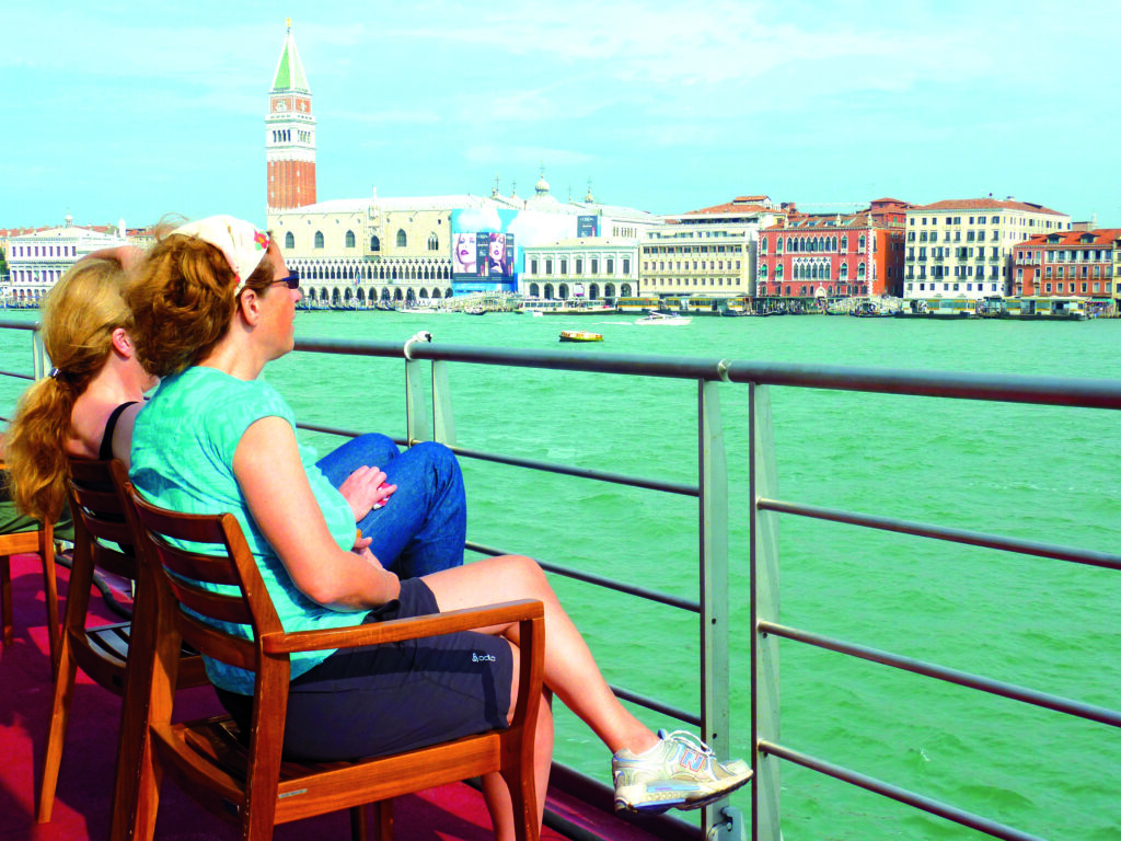 Zwei Personen sitzen auf einer Bank am Wasser in Venedig mit Blick auf den Markusplatz.